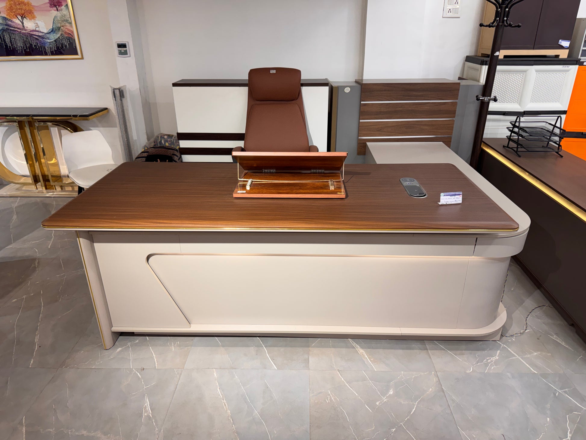 Modern office desk with wooden top and beige base in a showroom setting.